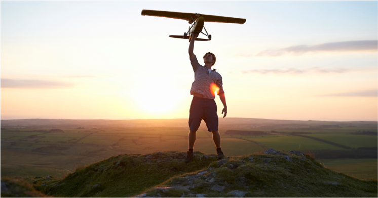 Person holding plane above head during sunset